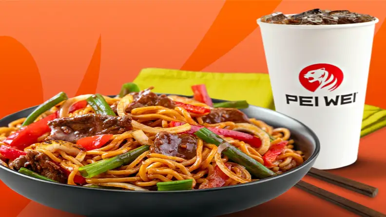 A bowl of beef noodle stir-fry next to a Pei Wei iced drink