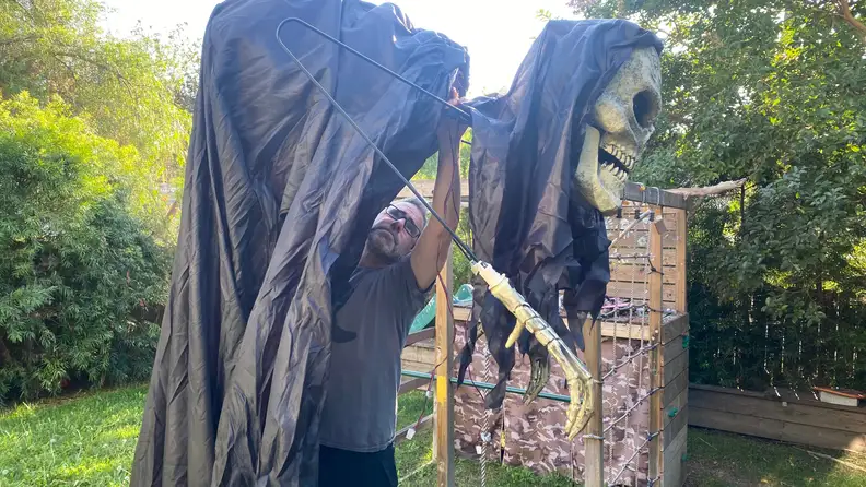 A half-built 6-foot tall Grim Reaper stands hunched in a yard. A treehouse is in the background.
