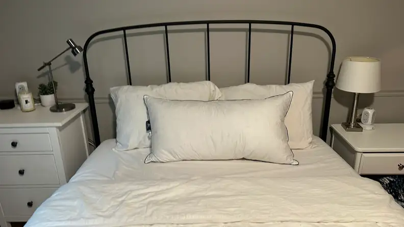 Pacific Coast Feather & Down Pillows shown on a bed with white sheets next to two white nightstands.