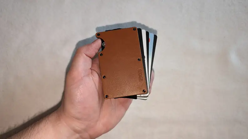 The Ridge Tobacco Leather wallet with cards sticking out of it being held in front of a white background.