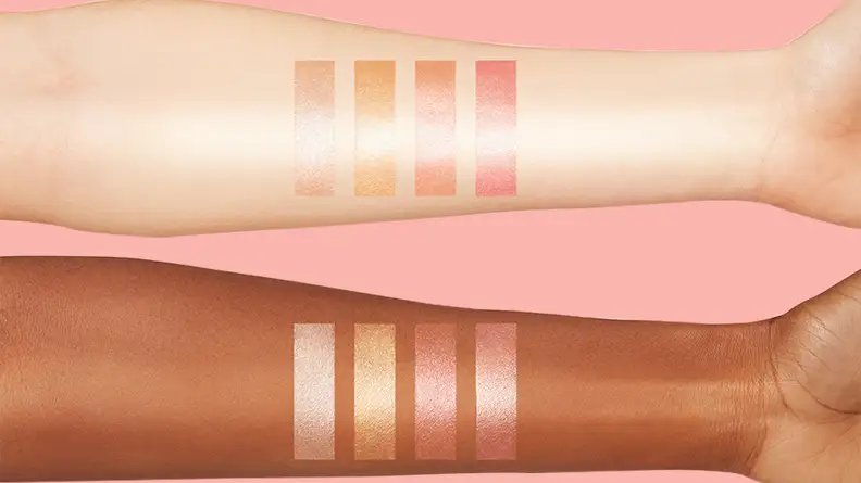 Two arms, one lighter and one darker in skin tone, with swatches of highlighter on them.