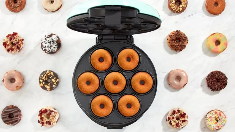 Mini donuts in the Dash Express Mini Donut Maker surrounded by an assortment of iced mini donuts.