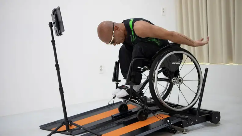 A man in a wheelchair lurches forward while using the Kangsters Wheely-X wheelchair treadmill.