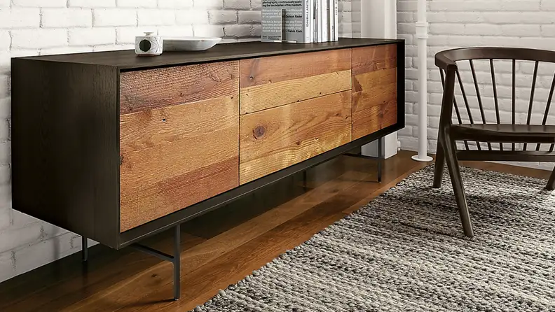 Reclaimed wooden TV console with black hardware on a wood floor next to a rug and chair