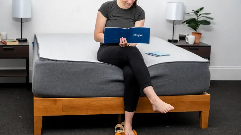 a woman sits on the edge of the casper select reading a brochure on the mattress