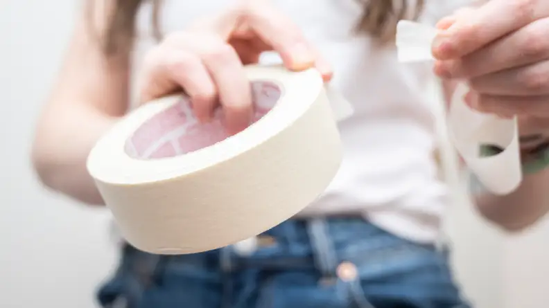 Person pulling white painter's tape off of roll