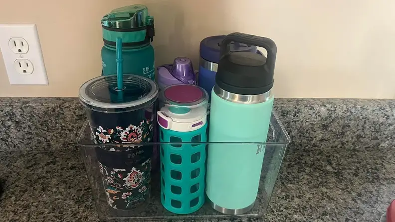 A clear plastic bin on a countertop with six water bottles of various sizes.