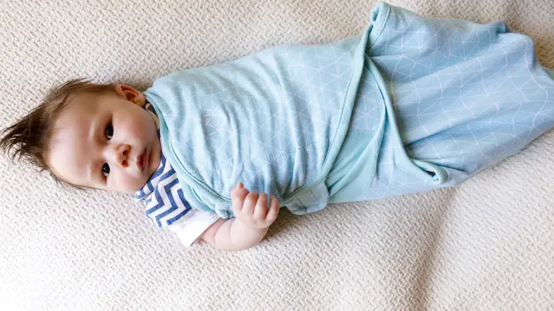Baby wrapped in a blue SwaddleMe baby swaddle.
