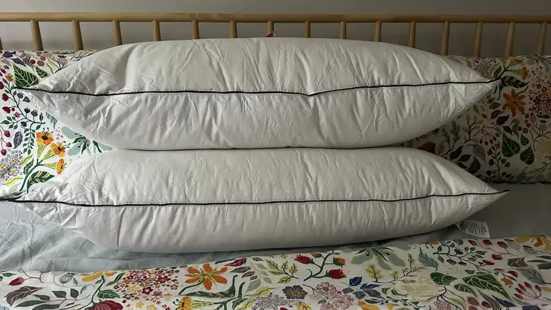 Two white Pacific Coast Feather & Down Pillows stacked on top of each other on a bed with floral sheets.