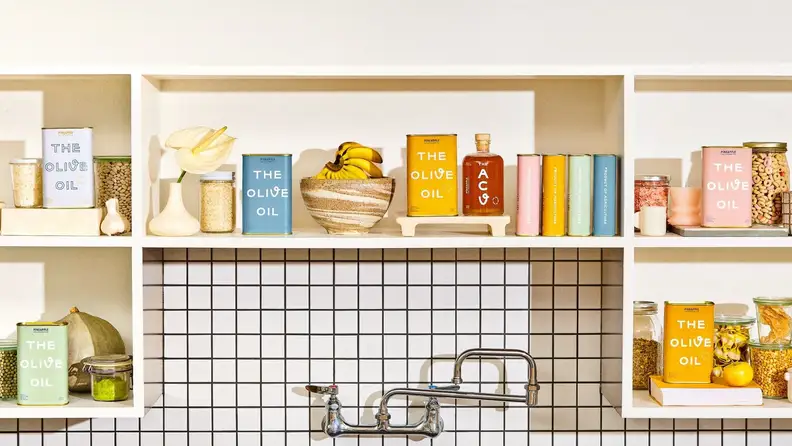 Open kitchen shelving filled with Pineapple Collaborative olive oil and other miscellaneous products.