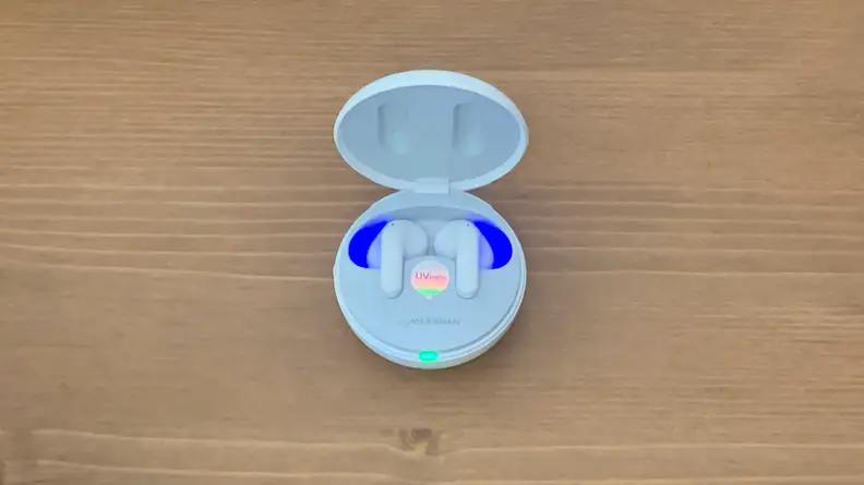 The interior of the open LG T90Q earbuds case glows blue as it sits on a wooden table.