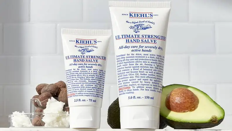 2 sizes of Kiehl’s Ultimate Strength Hand Salve on counter next to avocado