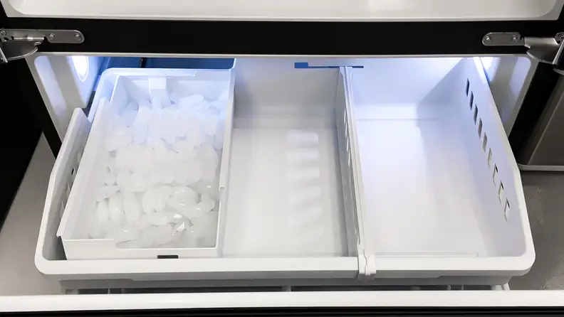 A shot peering down into the GE GNE27JSMAFSS French door refrigerator's freezer drawer. On the left side is a large bin filled with ice.