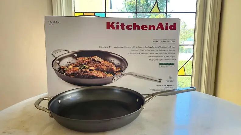 The KitchenAid Nitro Nitro Carbon Steel Fry Pan in front of its packaging.