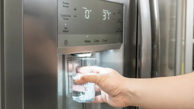 A hand reaches into frame, holding a glass against the water dispenser paddle on the front of the Frigidaire Gallery GRSC2352AF side-by-side refrigerator.