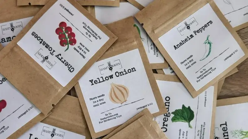 An image of a pile of seed packets, featuring seeds for yellow onions, cherry tomatoes, anaheim peppers, and more.
