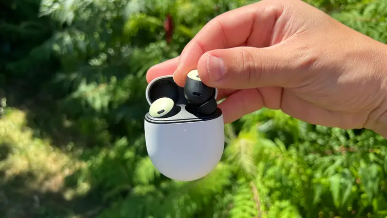 A hand holding one Pixel Bud Pro in the finger tips while also holding the case.
