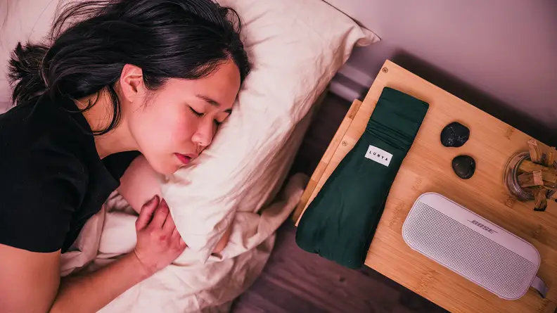 Person sleeps in bed next to nightstand with eye mask