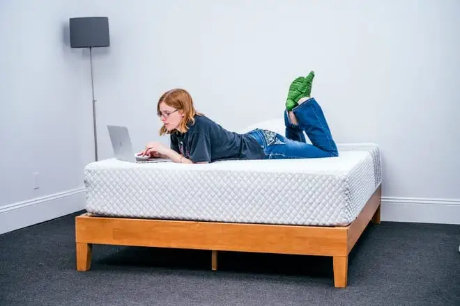 A person lies on a mattress on a bed frame.