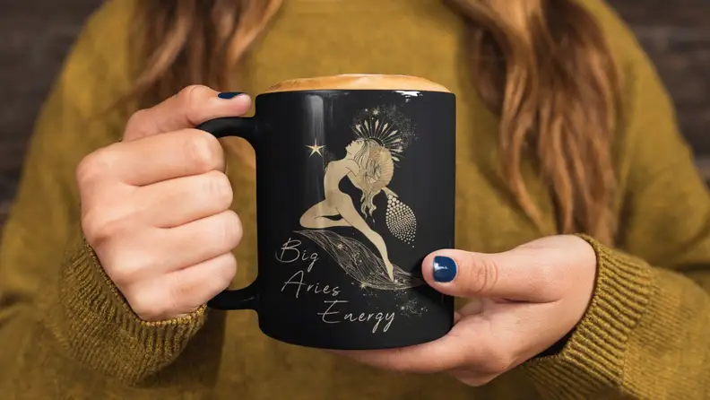A woman holds a mug that says, "Big Aries Energy," and it could be one of the best birthday gifts for Aries season.