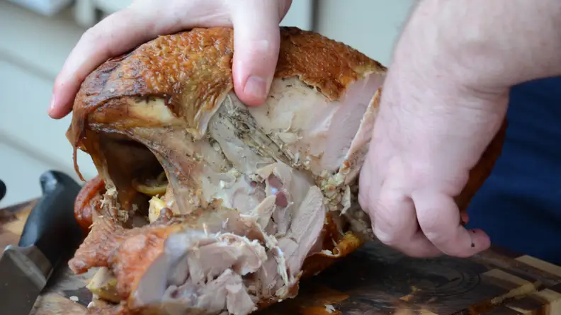 Two hands removing the wings from a cooked turkey.