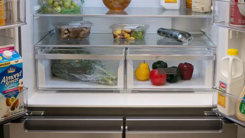 A close-up of the Whirlpool WRQA59CNKZ's crisper drawers. The fridge is fully stocked with food, and the crispers hold various fruits and vegetables.
