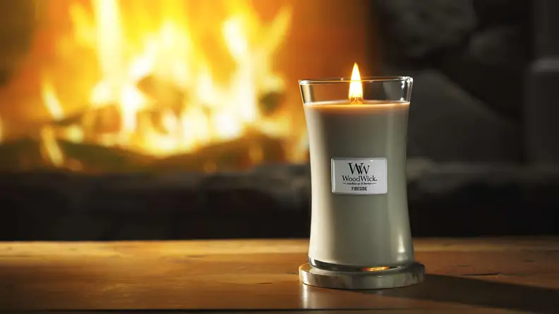 WoodWick candle burning in front of a fireplace
