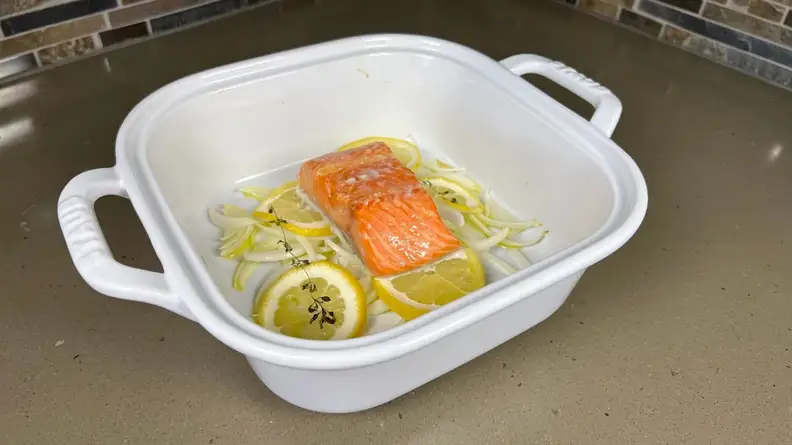 Thick piece of uncooked salmon with lemons inside of deep casserole dish.