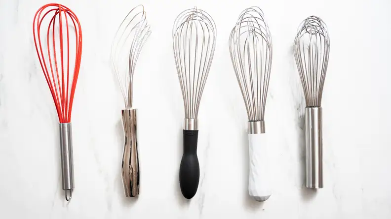 An assortment of whisks arranged on a marble countertop.
