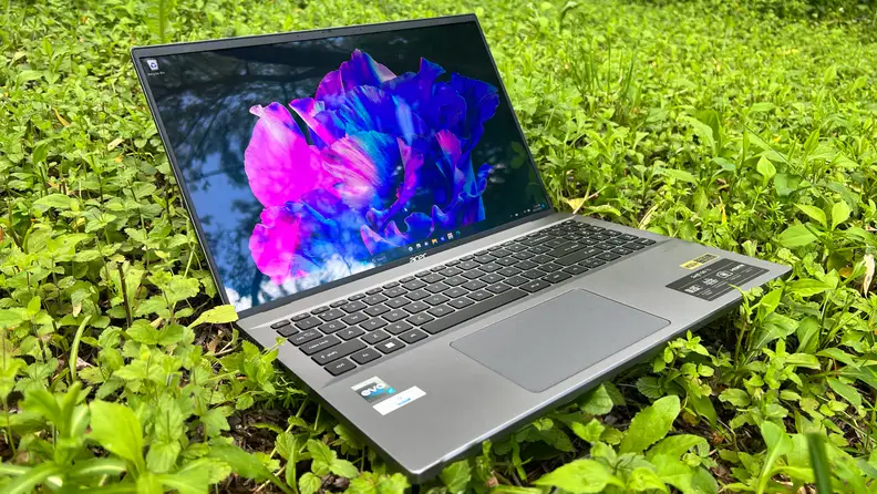 An open and powered on laptop showing a colorful screen, sitting on grass.