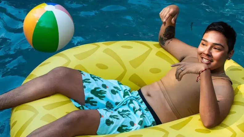 A human in a pool float, wearing a Flavnt binder and swim shorts.