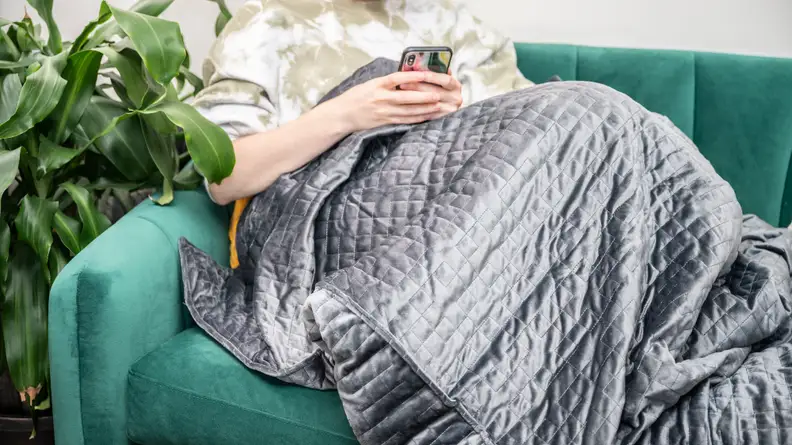 Person sitting on couch wearing blanket while looking at smartphone smartphone.