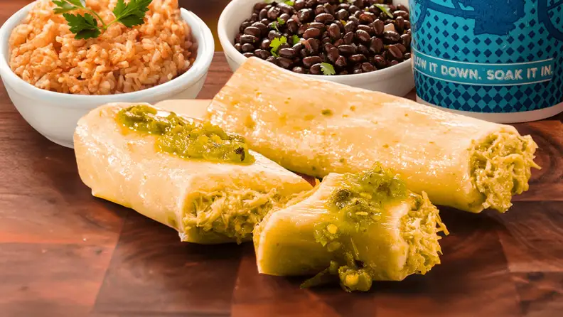 Two tamales topped with green sauce, next to rice and beans