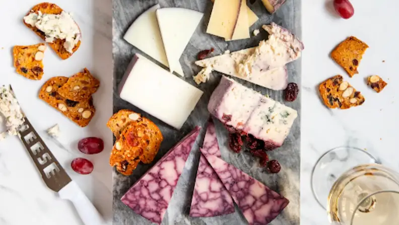 Cutting board with cheese, toasts and fruits. Also wines on the side.