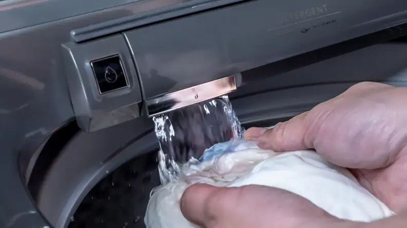 Someone is using the Maytag MVW8230HC top-load washer's built-in faucet to rinse a white towel.