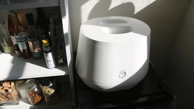 A Lomi composter sitting on a wine fridge near a cocktail shelf.