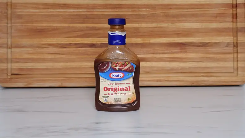A bottle of Kraft Original Barbecue sauce next to a wood cutting board.