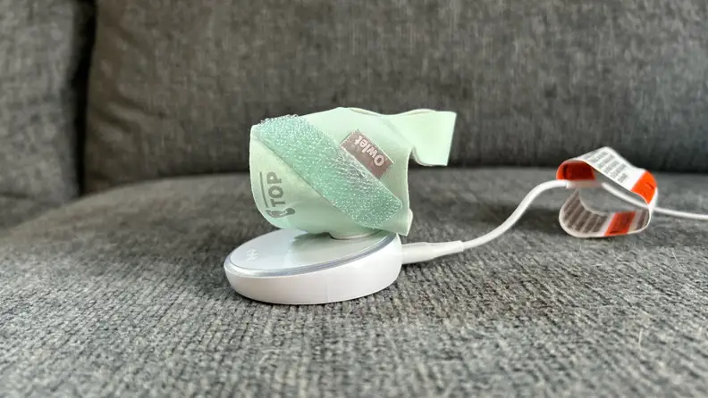 Mint green Owlet Dream Sock shown magnetically attached to white base station.