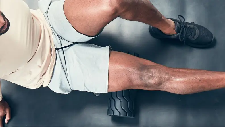 A man rolling his hamstring with the Therabody Wave Roller.