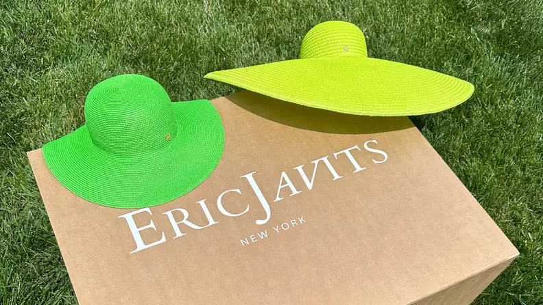 A green and neon green hat lay on top of an Eric Javits cardboard box.