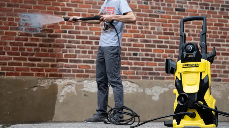A person sprays a brick wall with the Karcher K4 pressure washer.