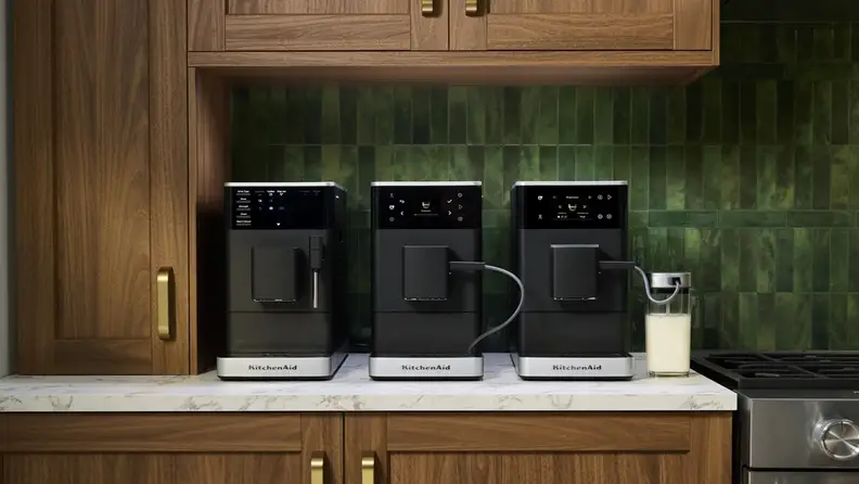 Three black KitchenAid espresso machines on a counter with green tile backsplash