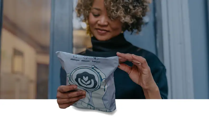 Smiling woman holding a recyclable coffee mailer bag with a latte art logo