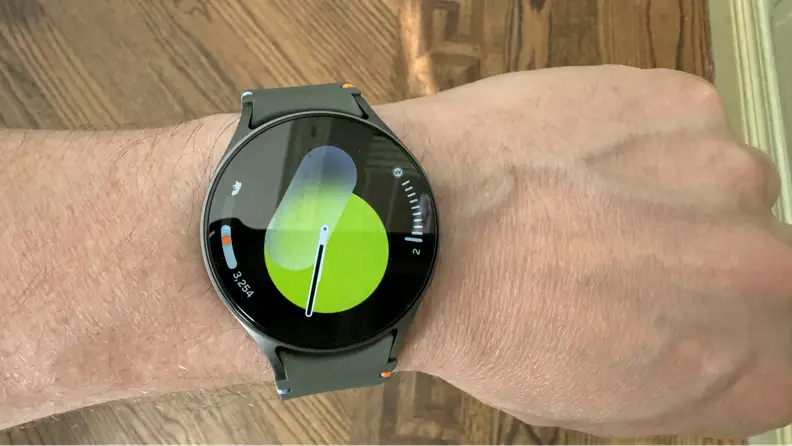 A wrist wearing the smartwatch displaying a green screen.