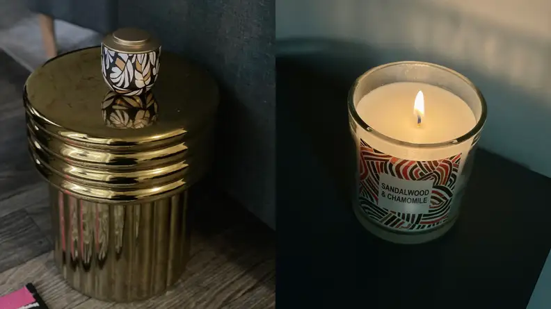 Black and gold candle sitting atop a gold end table. Lit Sandalwood & Chamomile candle by Tabitha Brown for Target