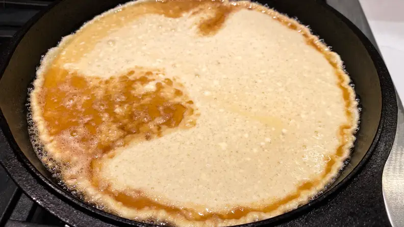 Batter for a Dutch baby begins to cook in a cast-iron skillet.