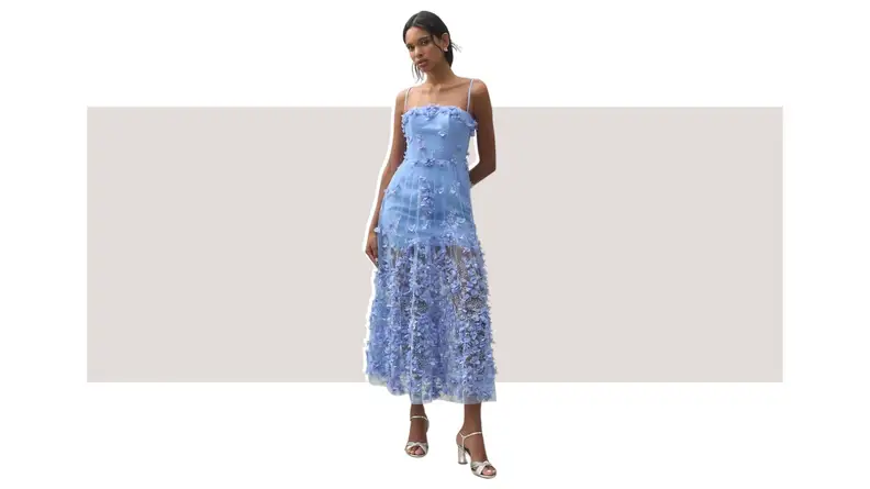 A model wearing a blue dress with applique flowers and sheer fabric throughout.