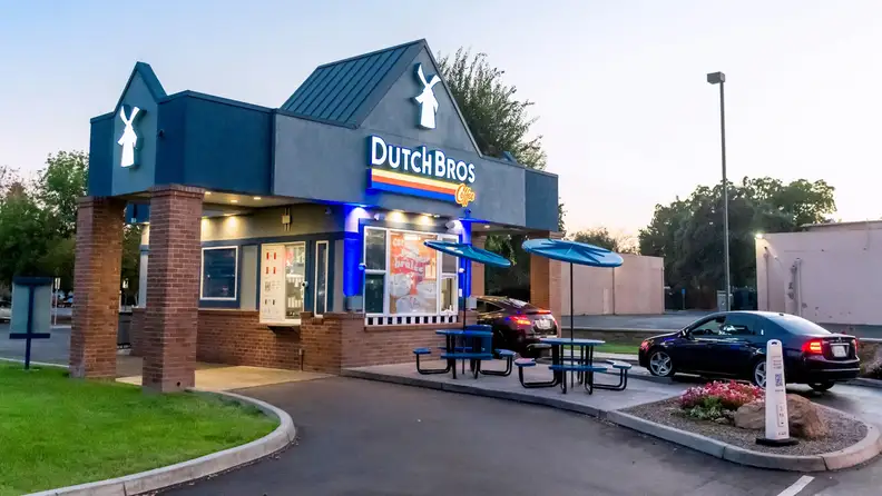 Dutch Bros Coffee drive thru stand with cars lined up at dusk