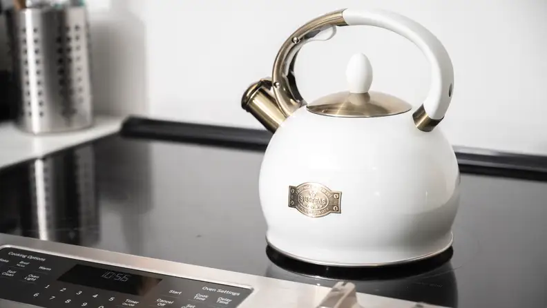 A white Susteas tea kettle sits atop a glass-top stove.