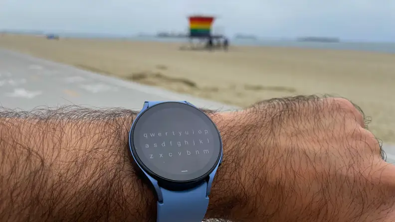 A powered-on smart watch with a light blue wristband wrapped around a person's wrist